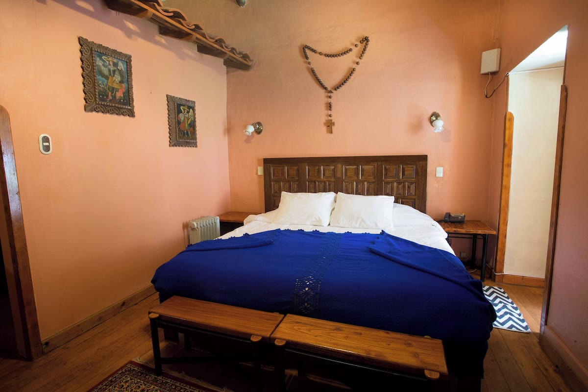 Un dormitorio con una cama de madera, una colcha azul y un banco de madera al pie de la cama.