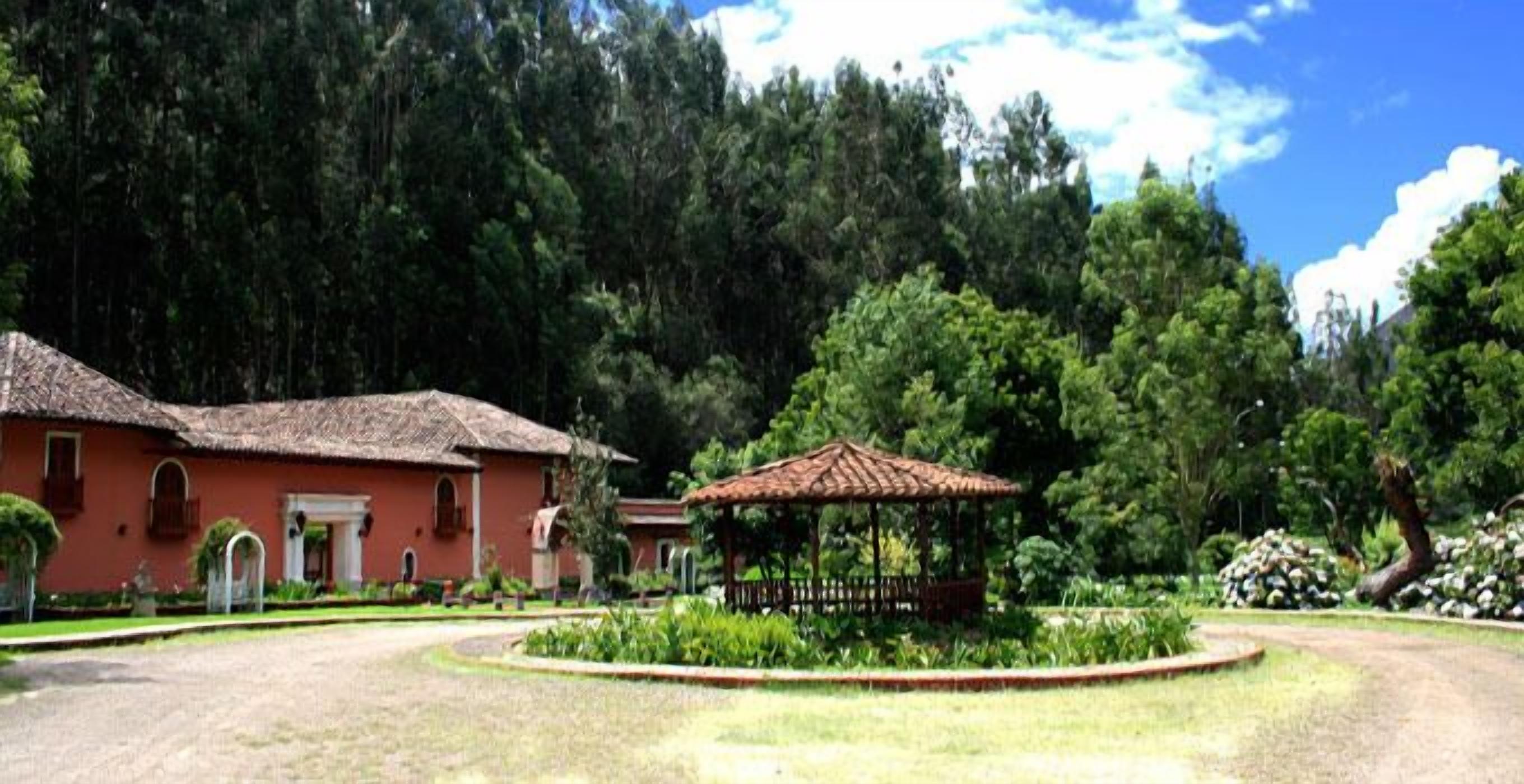 A building with a red facade and a thatched roof, surrounded by a well-maintained garden with a gazebo.