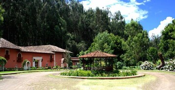 A building with a red facade and a thatched roof, surrounded by a well-maintained garden with a gazebo.