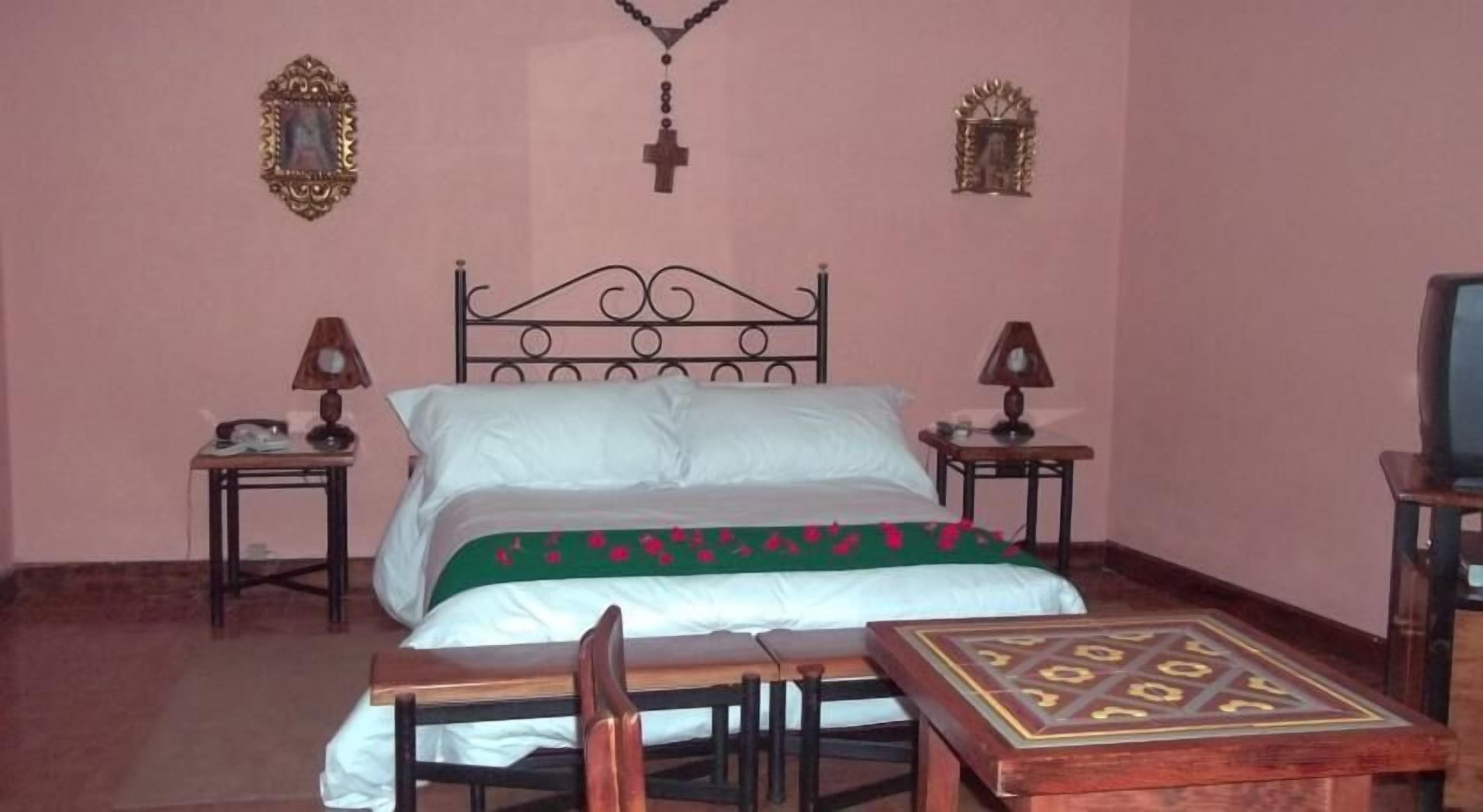 A bedroom with a single bed, two bedside tables, a wooden chair, and a small table with a decorative pattern.