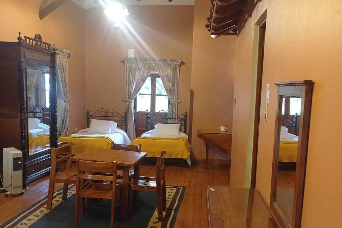 Habitación de hotel con dos camas, una mesa de madera, una silla, una mesita con una taza y un espejo.