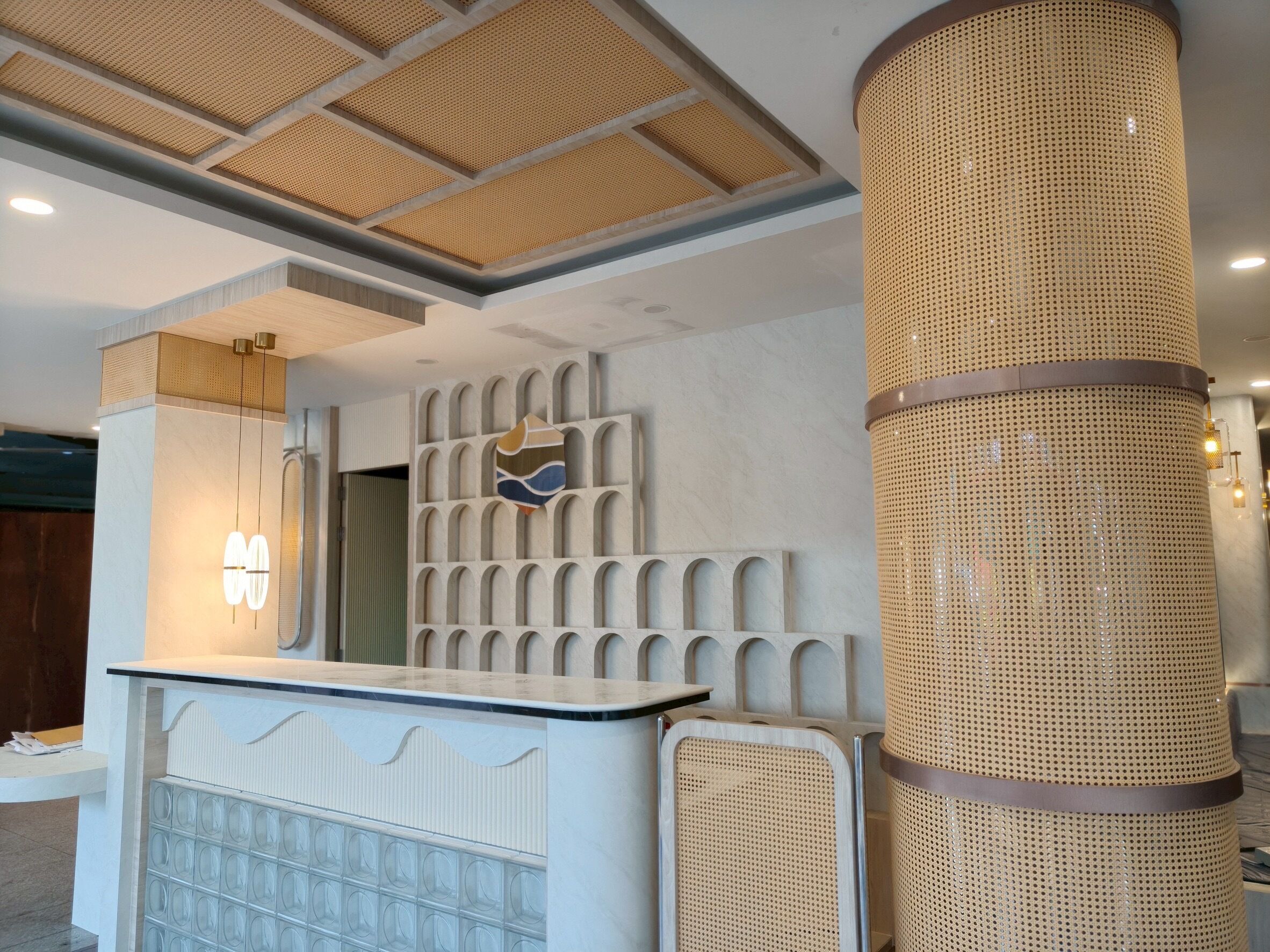 A reception area with a modern design, featuring a reception desk, a decorative wall with geometric patterns, and a large woven column.