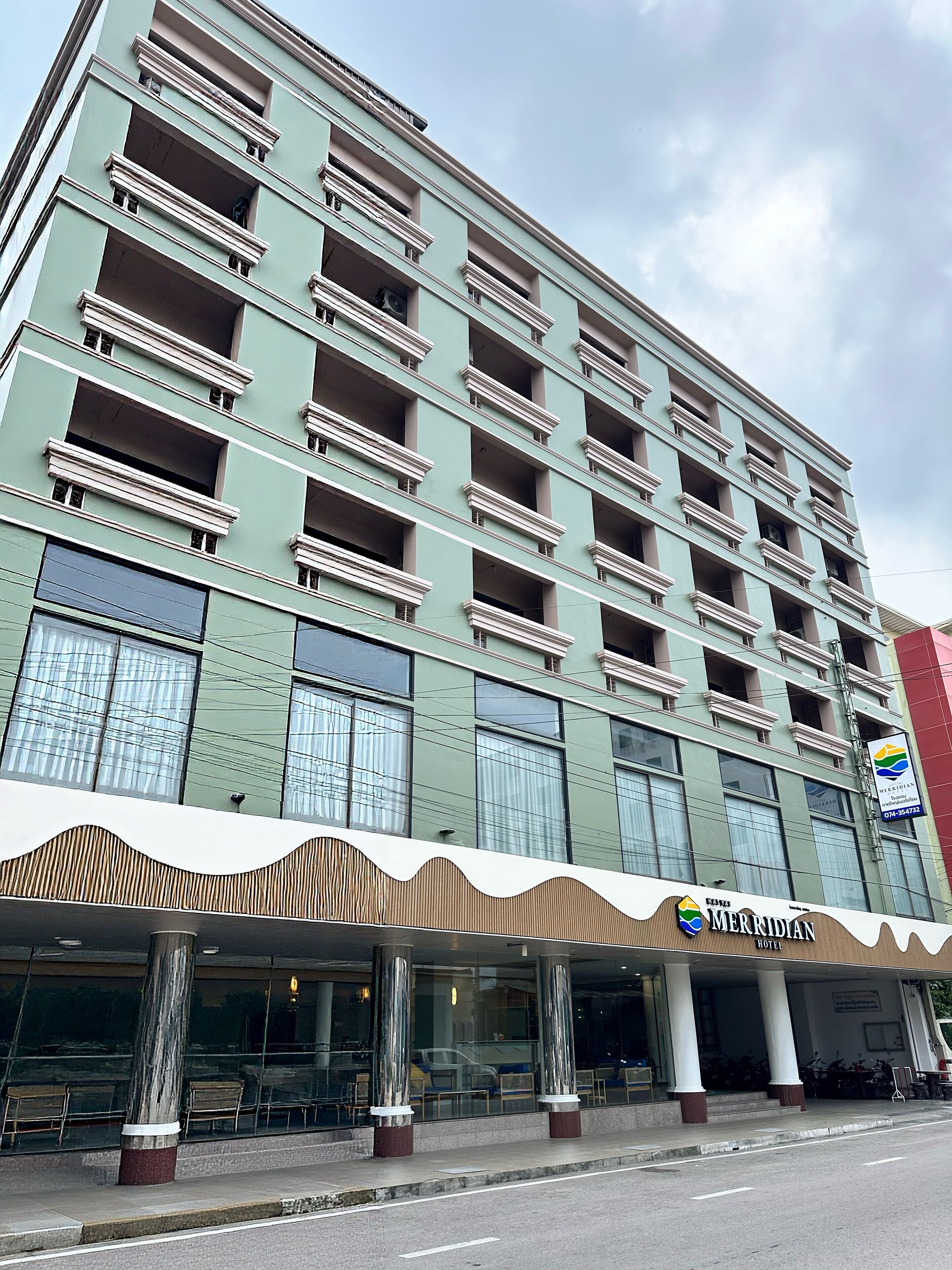 A multi-story hotel with a green facade, large windows, and a covered entrance area with seating.
