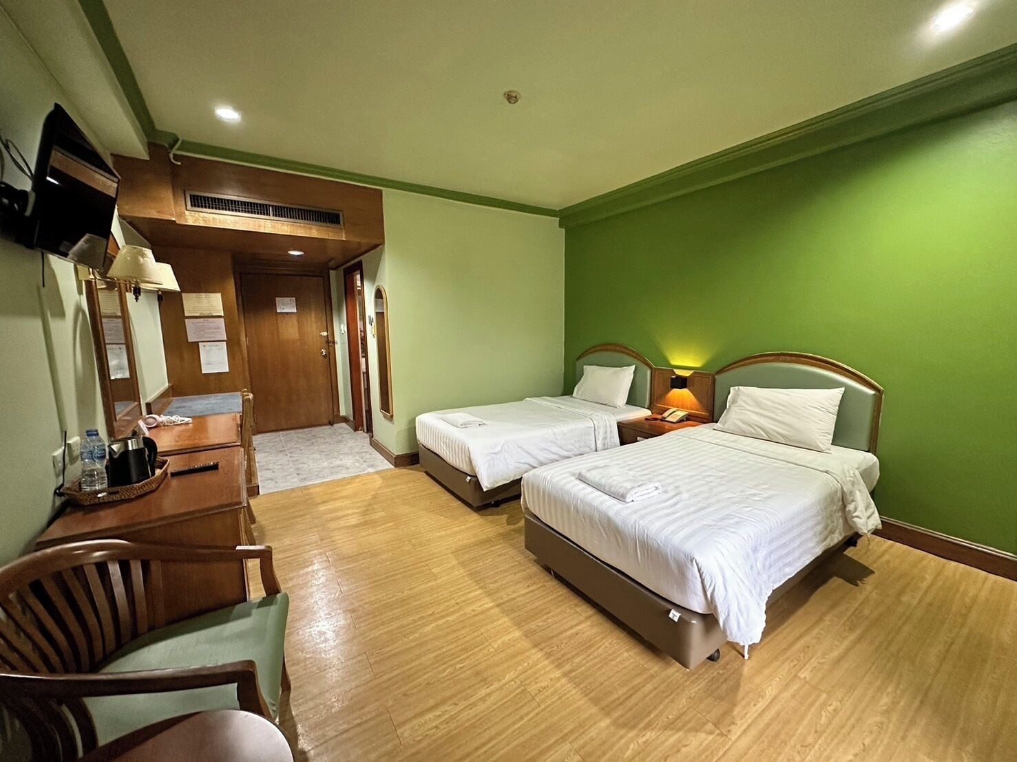 A hotel room with two beds, a desk with a chair, a TV mounted on the wall, and a wooden floor.
