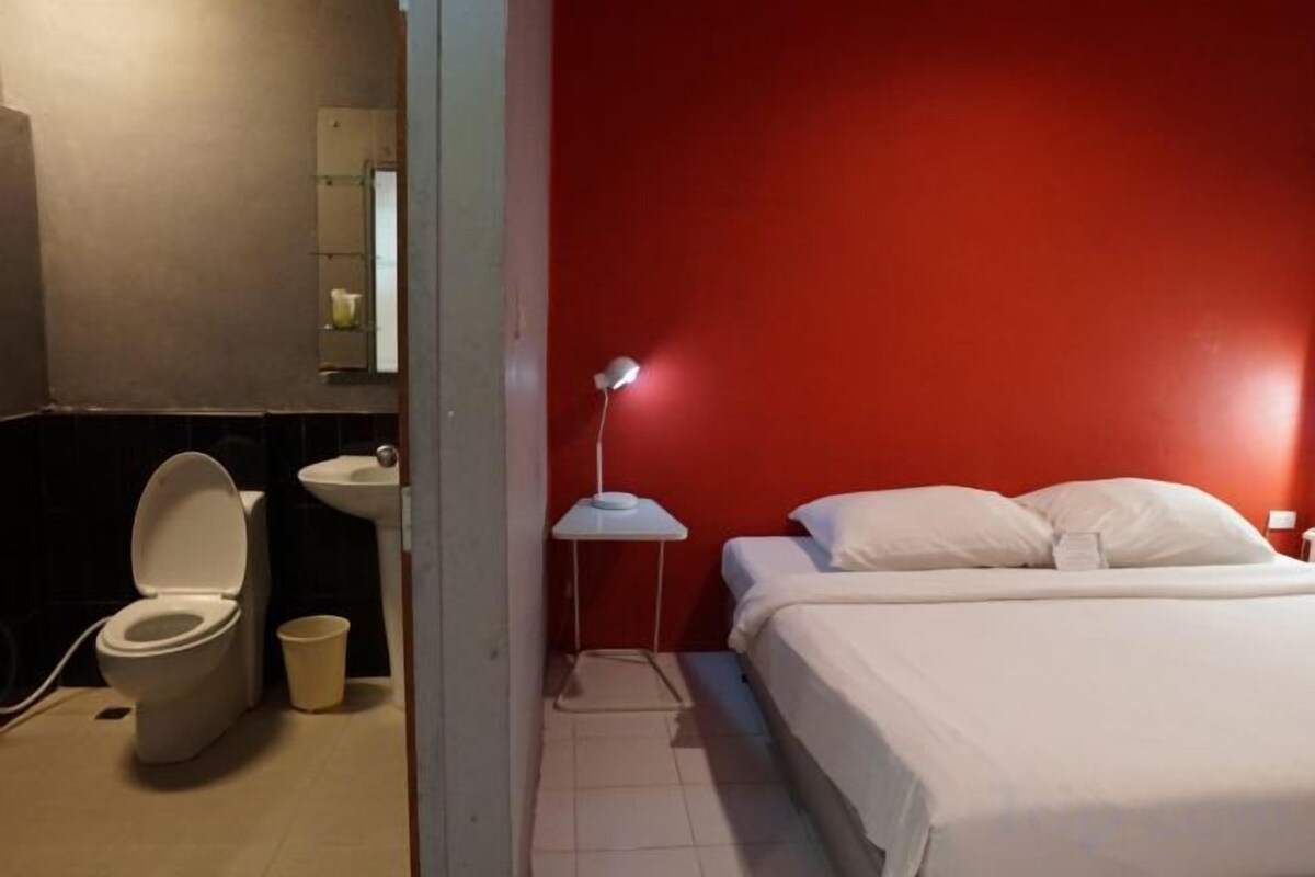 A hotel room with a bed, a bedside table, a nightstand, a lamp, a toilet, and a sink.