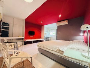 Habitación de hotel con cama, escritorio, silla, televisor y aire acondicionado.