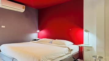 A bedroom with a bed, an air conditioner, a nightstand, a lamp, and a small table.