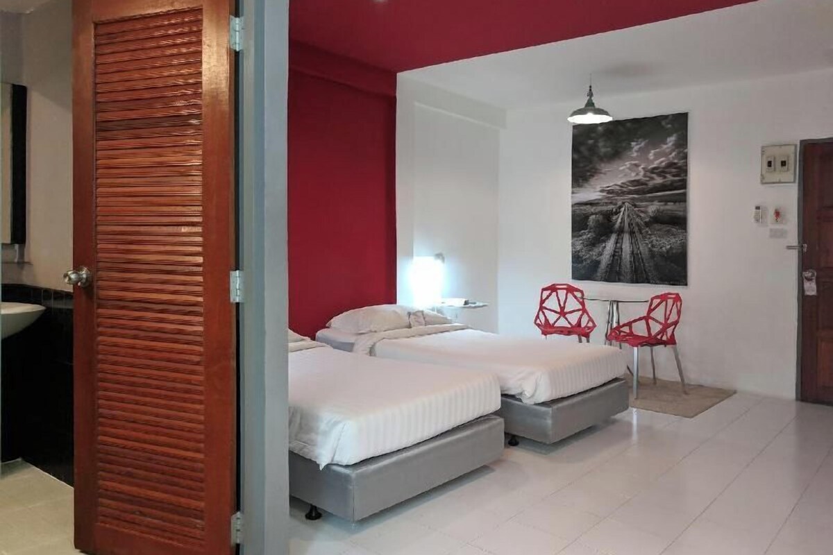 Une chambre d’hôtel avec deux lits, un mur d’accent rouge, un tableau, un bureau et une chaise.