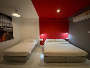 Habitación de hotel con dos camas, una pared de acento roja, una lámpara de techo y un aire acondicionado instalado en la pared.
