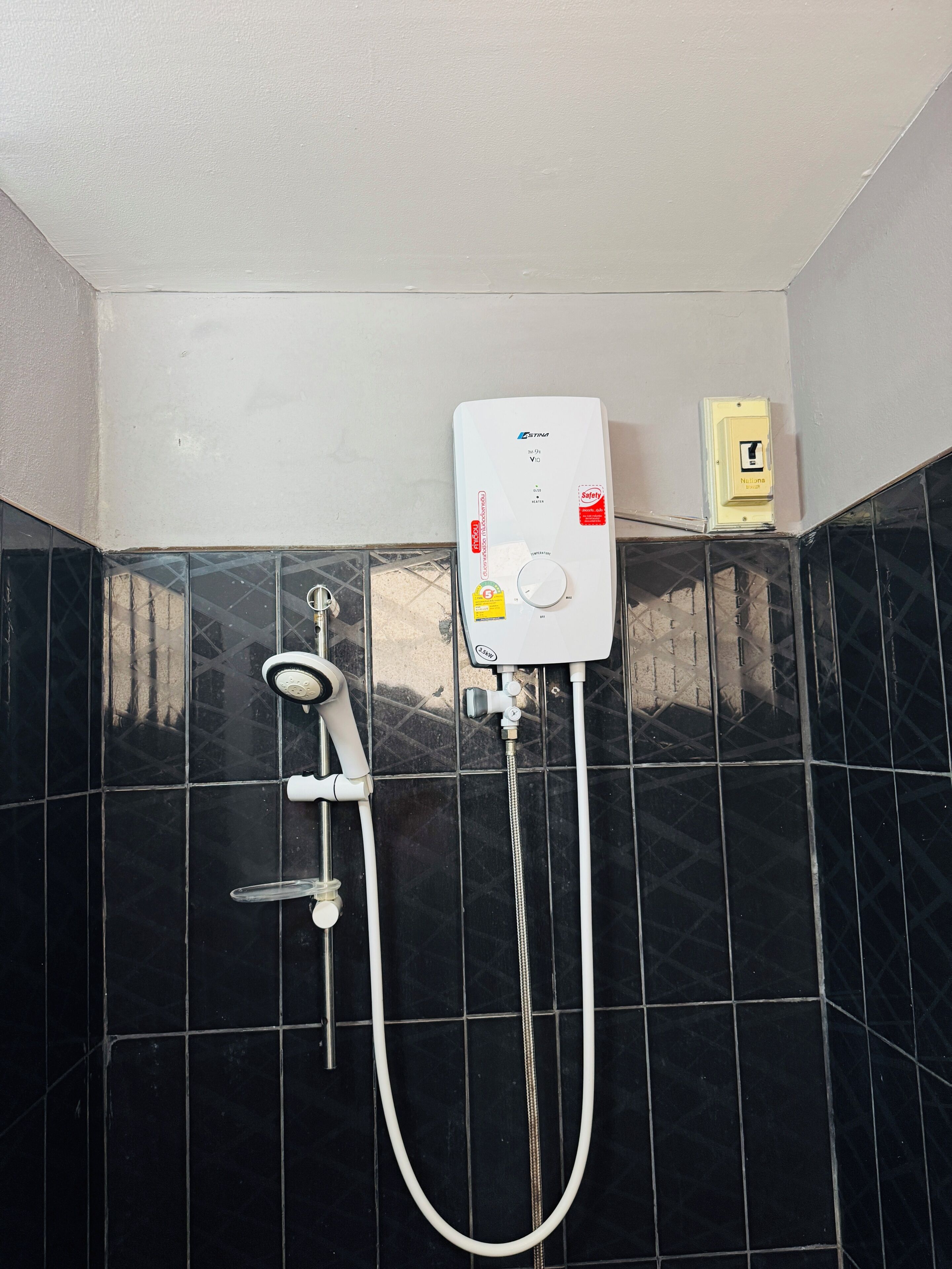 Ein Badezimmer mit schwarzem Fliesenbelag, einer weißen Duschkabine und einem sichtbaren Stromanschluss.