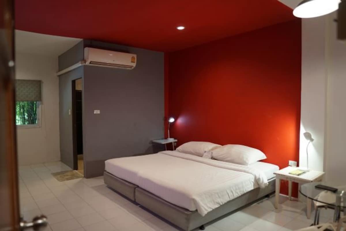 A bedroom with a bed, bedside table, lamp, and an air conditioning unit.