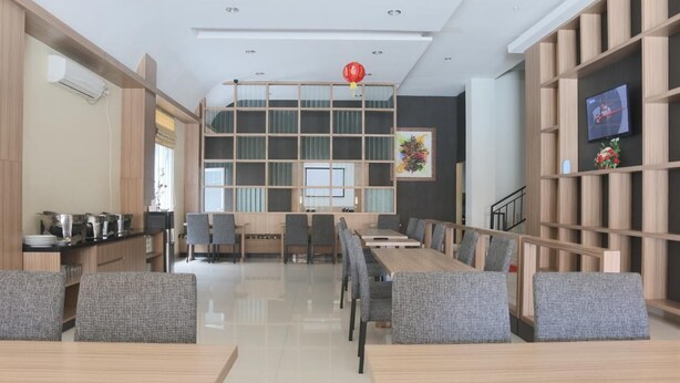 A modern dining area with wooden tables and chairs, a central seating area, and a TV mounted on a wooden panel wall. - Miracle Hotel Manado (Manado)