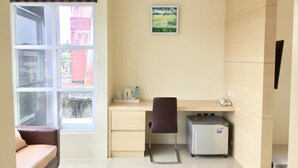 A small, clean room with a desk, chair, and a small heater. There is a window with a view of buildings outside. - Miracle Hotel Manado (Manado)