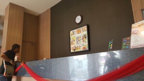 A hotel reception desk with a clock, a colorful artwork, and a red ribbon. - Miracle Hotel Manado (Manado)