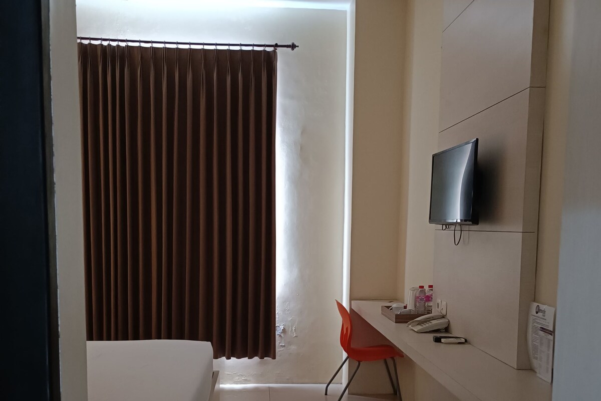 Una camera d'albergo con un letto, una scrivania, un televisore a parete e una tenda.