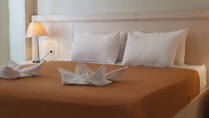 A neatly made bed with white pillows and a brown bedspread, a bedside lamp, and a decorative swan-shaped pillow on the bed. - Miracle Hotel Manado (Manado)