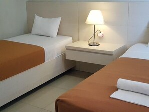 A hotel room with two beds, a nightstand with a lamp, and a white pillow. - Miracle Hotel Manado (Manado)