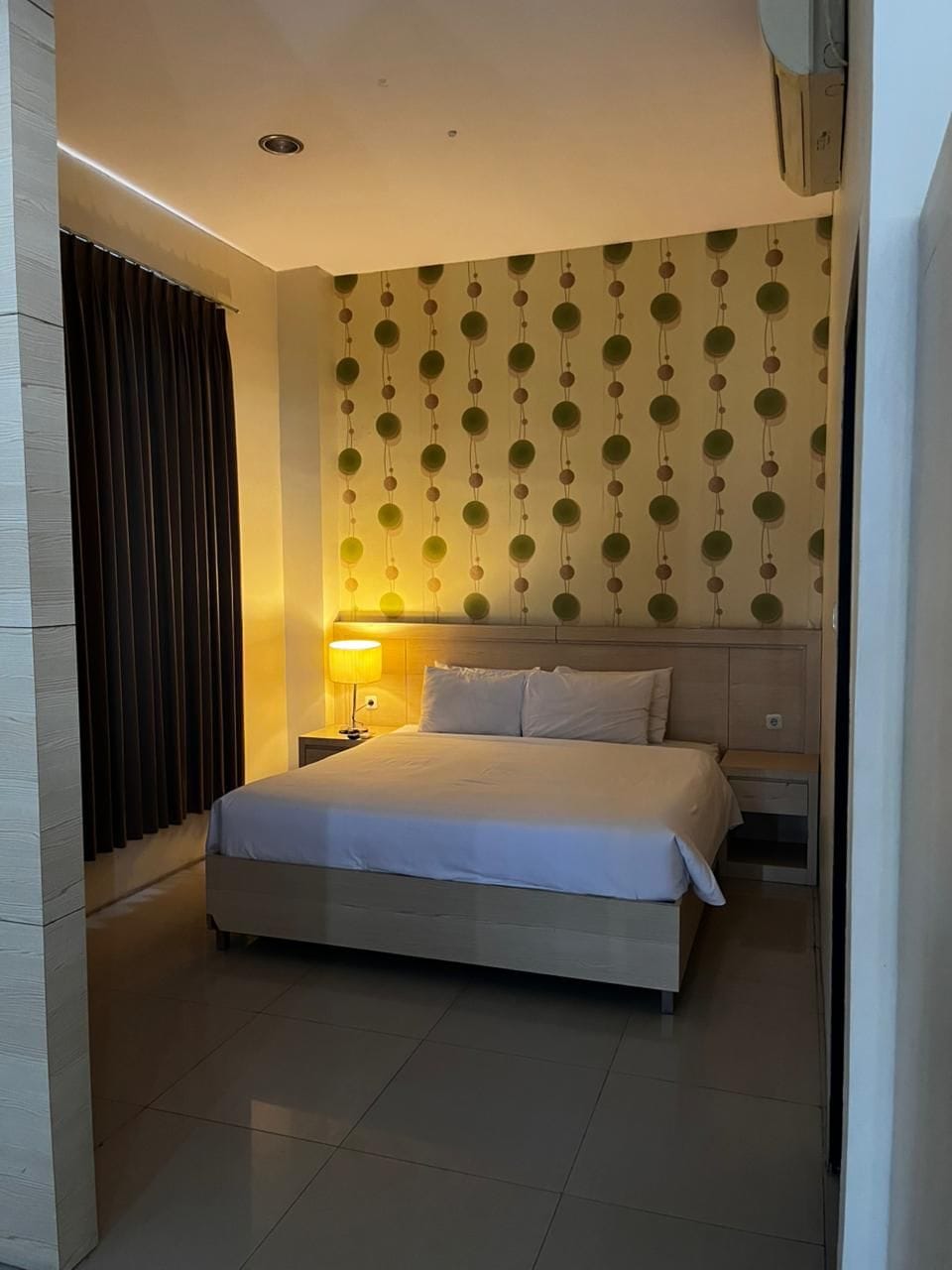 Une chambre d’hôtel avec un lit, des tables de chevet, une lampe et un mur décoré d’un motif.