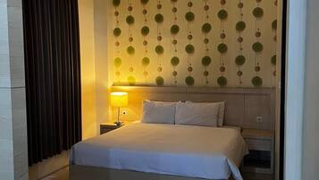 Habitació d'hotel amb llit, taules de nit, làmpada i un mur amb dibuixos.