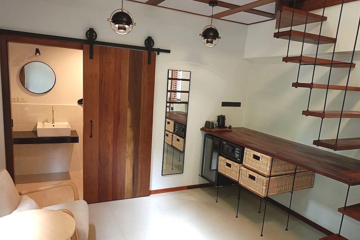 Une cuisine moderne avec un plan de travail en bois, un évier et un miroir. On aperçoit une chaise et une table au premier plan.