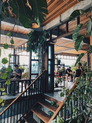 Un espacio interior con vigas de madera, ventanas amplias y abundante vegetación.