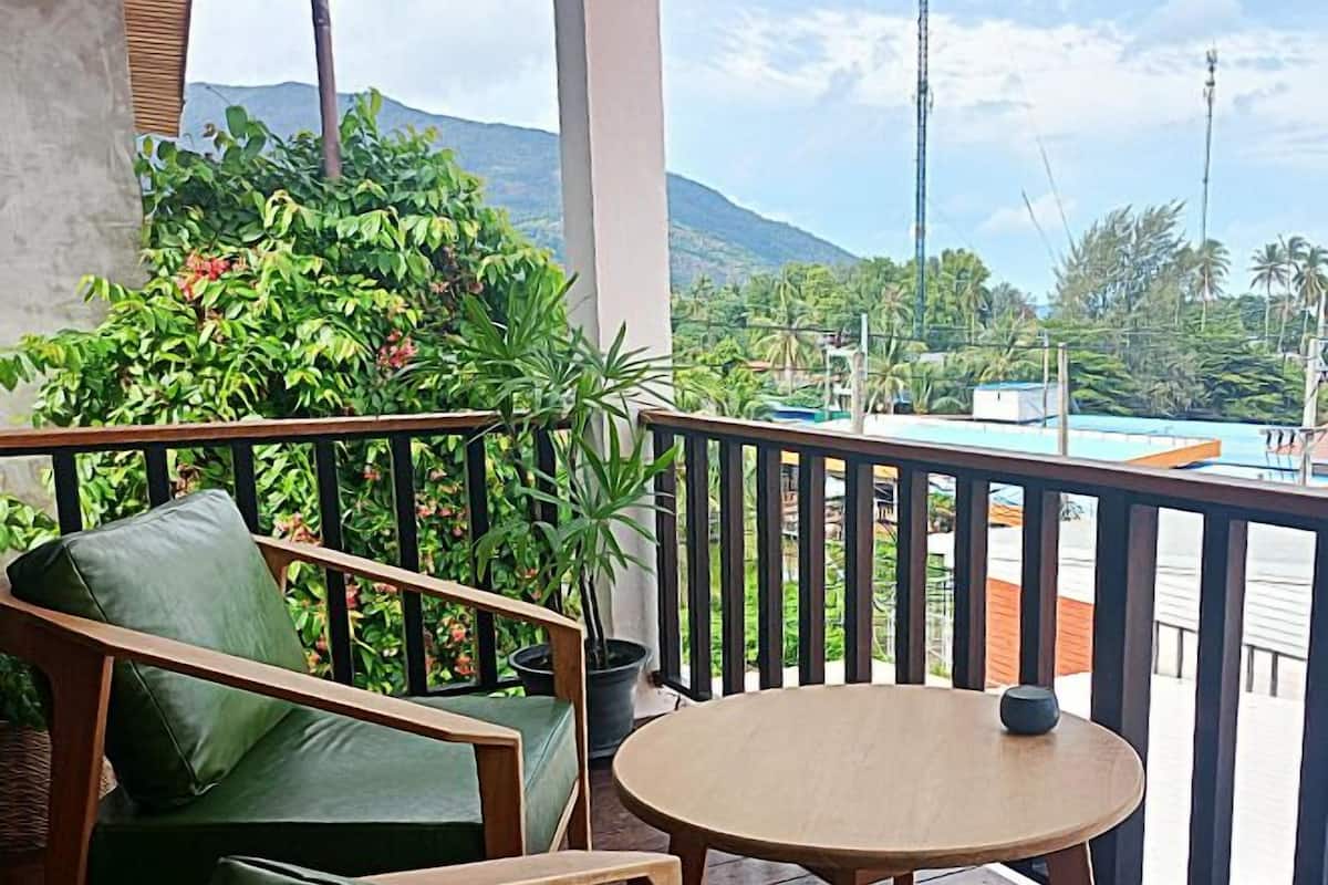 Un balcon agrémenté d’un canapé en bois et d’une petite table ronde, entouré d’une végétation luxuriante et offrant une vue sur un paysage montagneux.