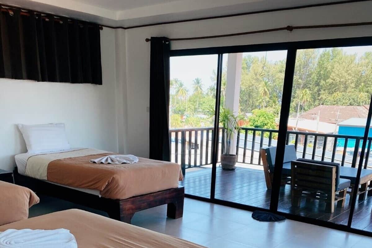 Une chambre d’hôtel avec deux lits, un balcon donnant sur des palmiers et un coin repas avec des sièges en plein air.