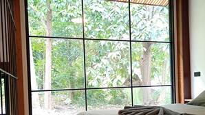 Un dormitorio con un gran ventanal, una cama y piso de madera.