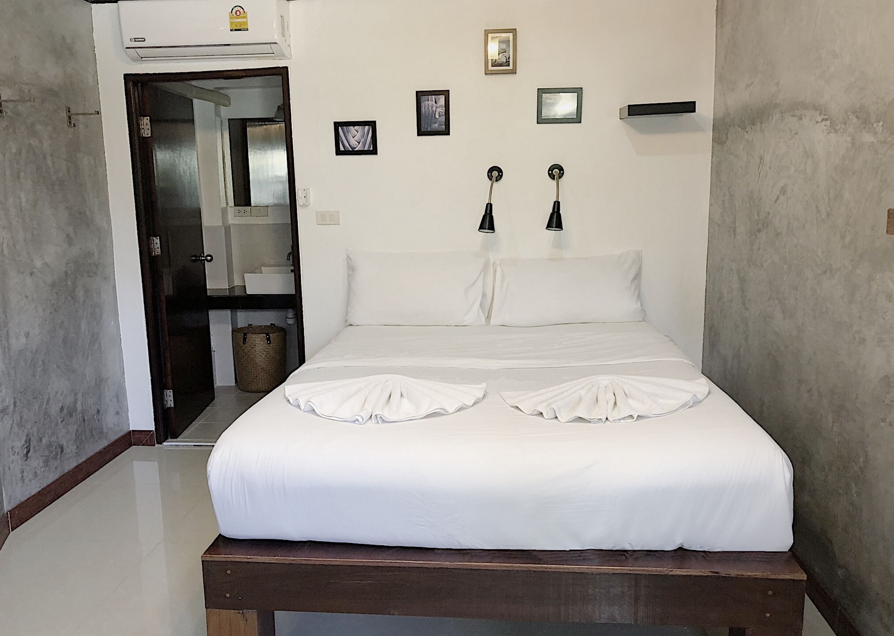A neatly made bed with a wooden headboard, a small bedside table, and a wall-mounted air conditioning unit.