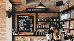 Un café con un muro de ladrillo, un cartel con el menú y una pizarra anunciando opciones de pastel.