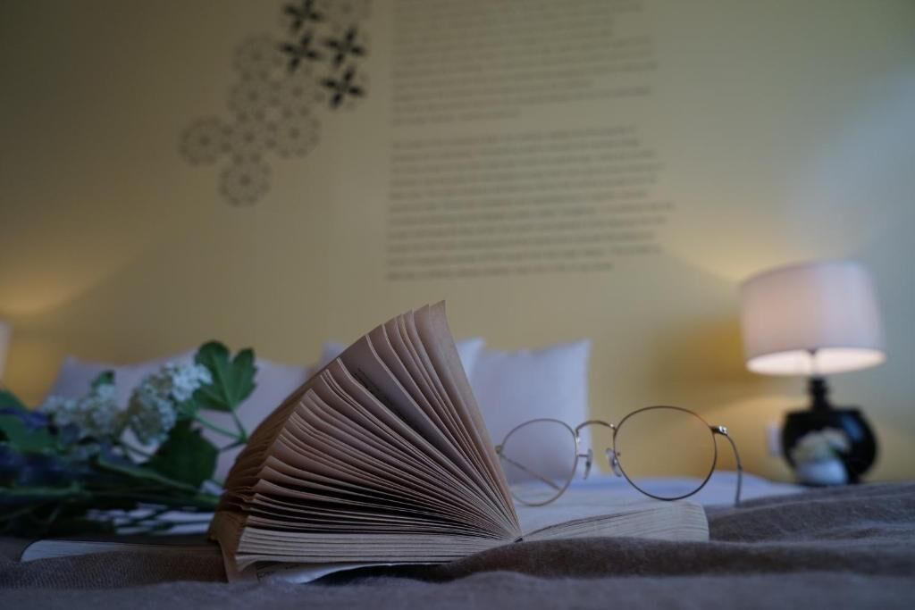 An open book on a bed with a pair of glasses beside it.