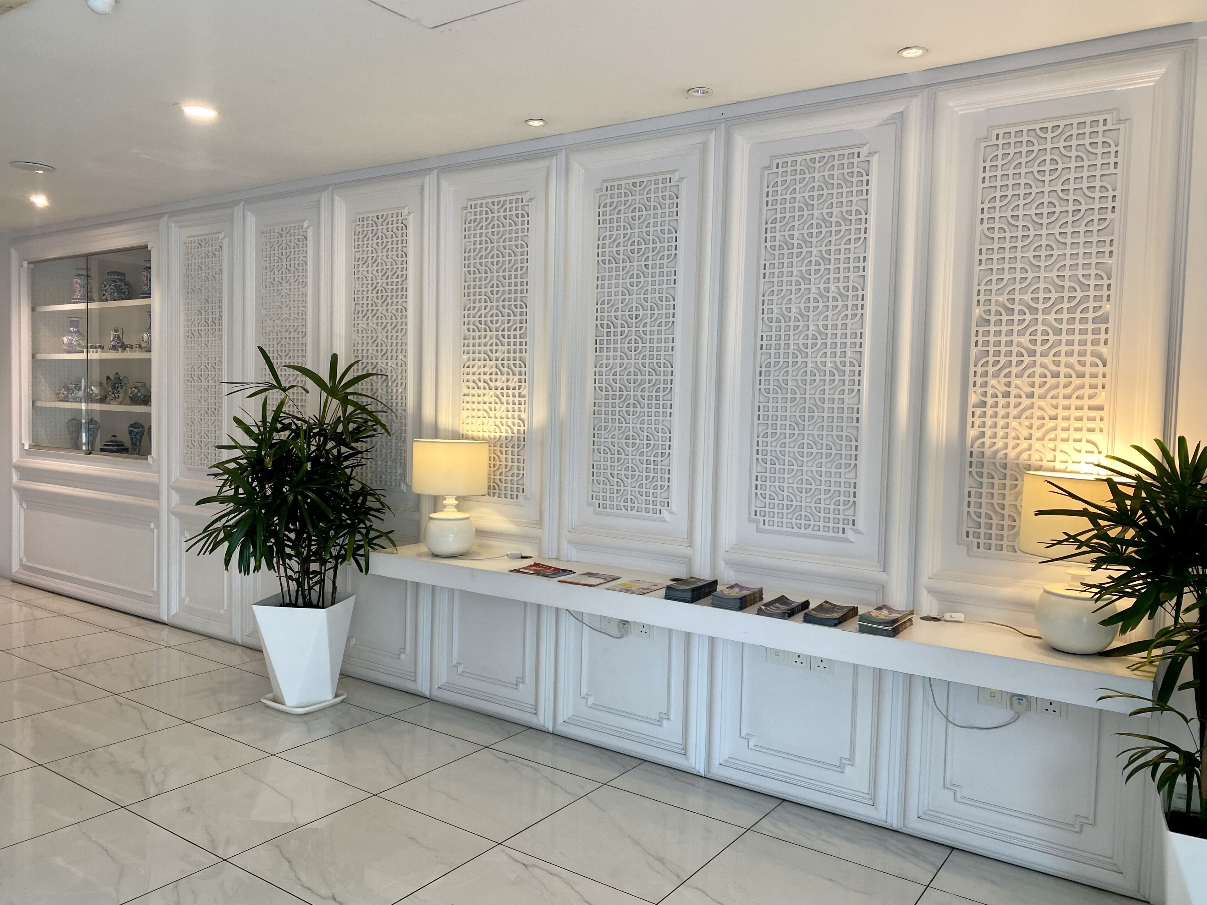 A reception area with a white console table displaying books and decorative items, flanked by ornate white panels and a potted plant.