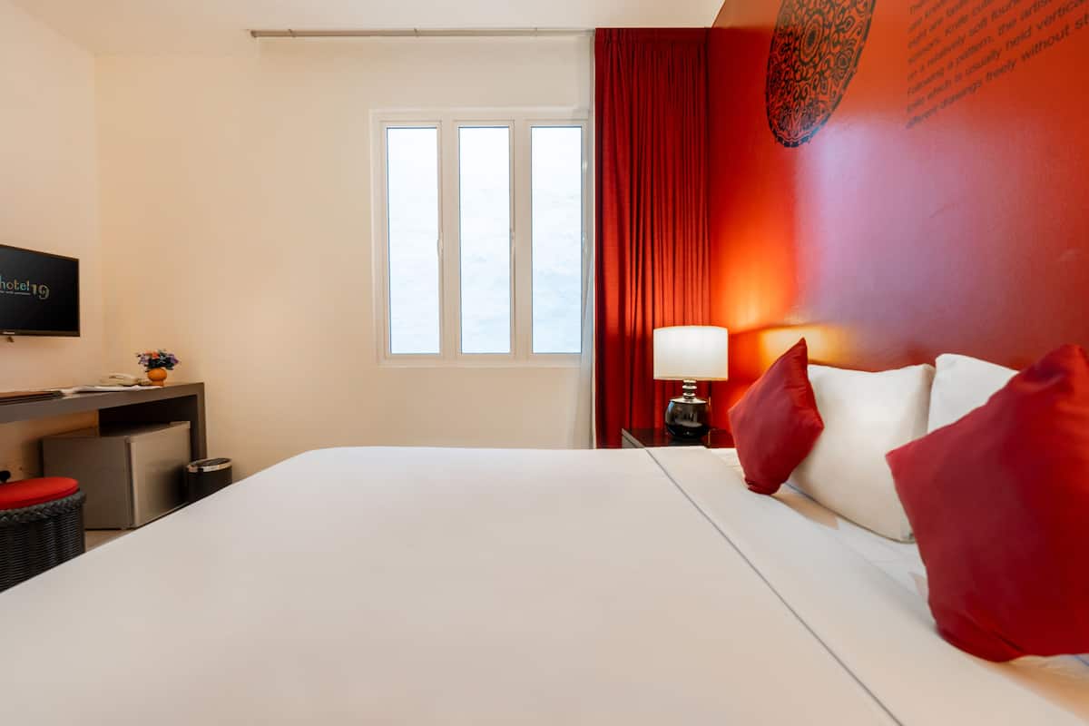 Una habitación de hotel con una cama grande, un escritorio con computadora, televisión y ventana con cortinas.
