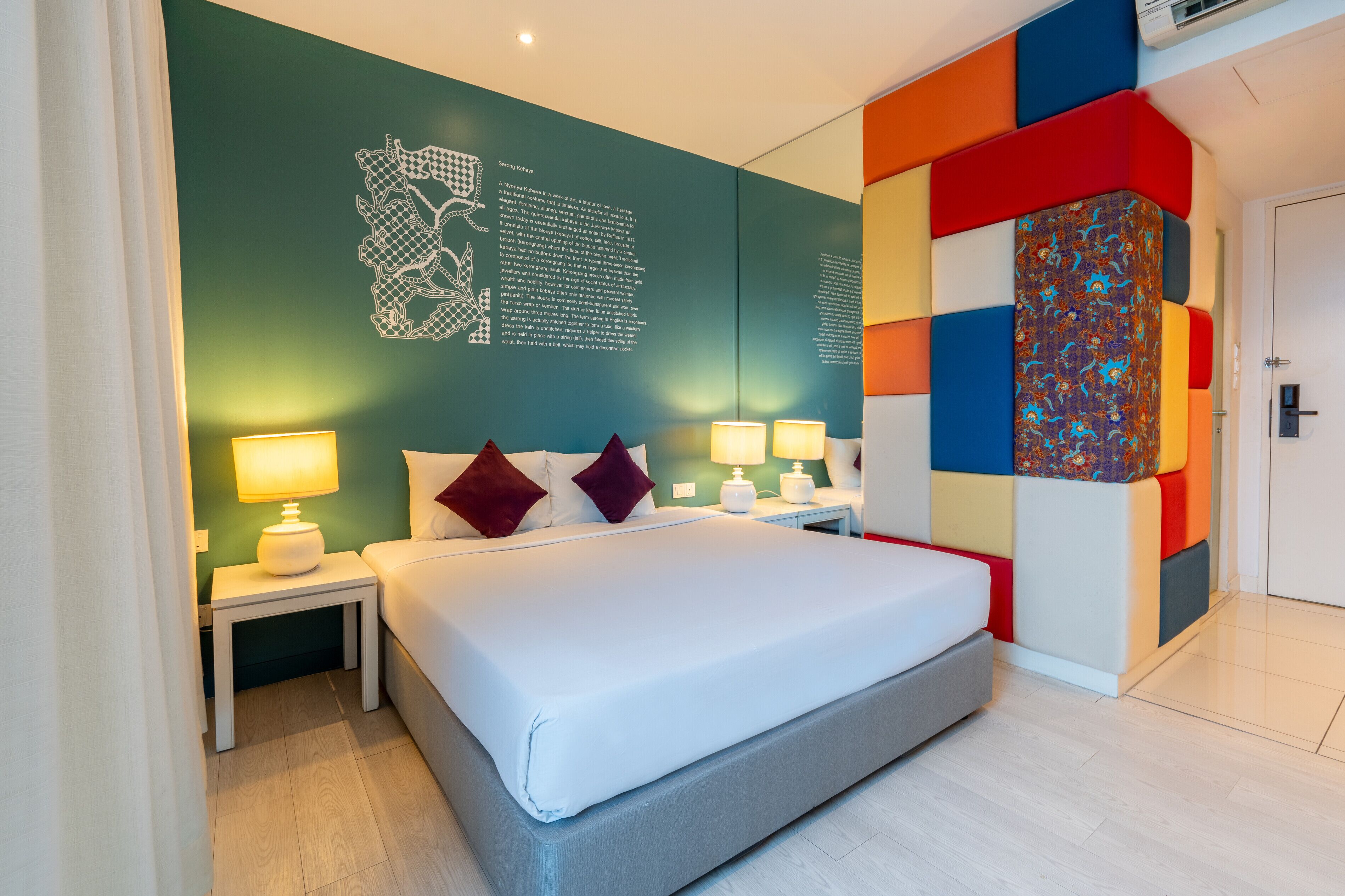 Et moderne hotelværelse med en stor seng, to sengeborde med lamper, en dekorativ vægdekoration og en farverig accentvæg.