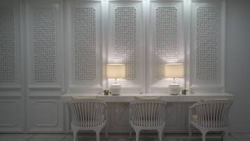 A room with a white desk and two chairs, a wall with intricate patterns, and two lamps.