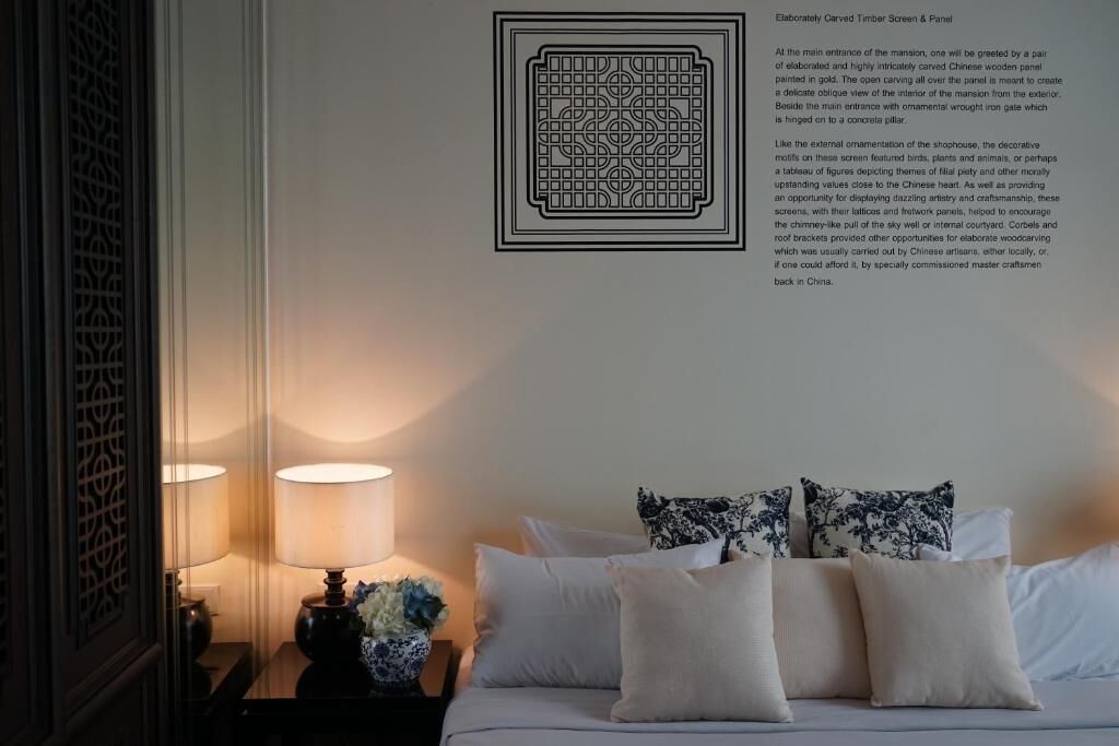 Et soveværelse med en seng, puder, et natbord med en lampe og et vægmonteret display der viser et udskåret trædesign.