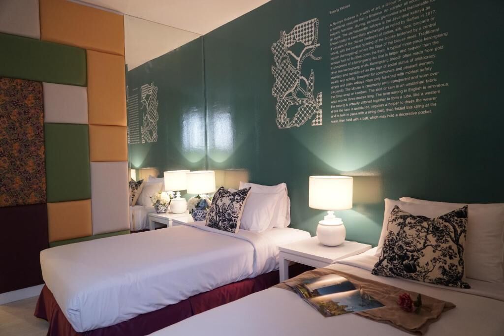 A hotel room with two beds, white bedding, and decorative pillows. There are bedside tables with lamps and a wall with a geometric pattern.
