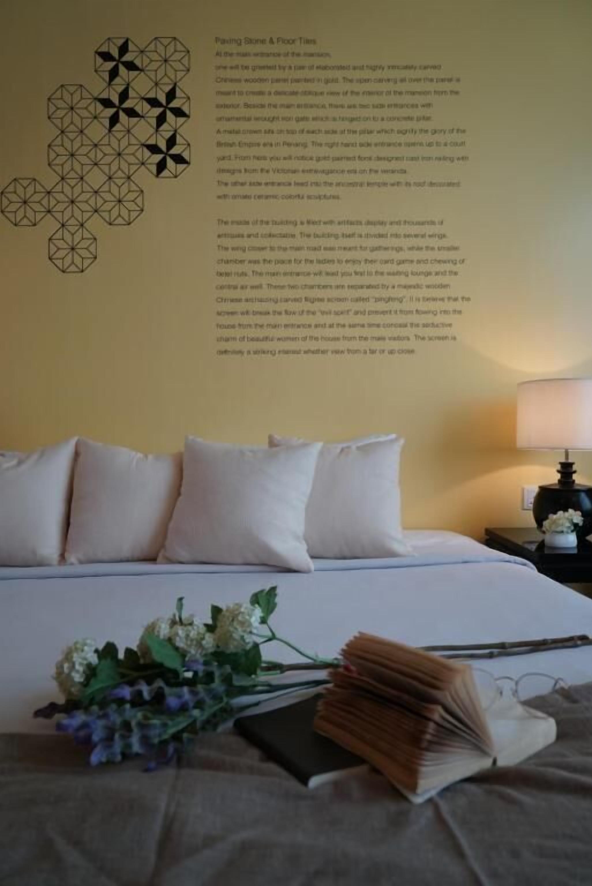A neatly made bed with pillows and a book, a vase of flowers, and a wall with a geometric pattern.