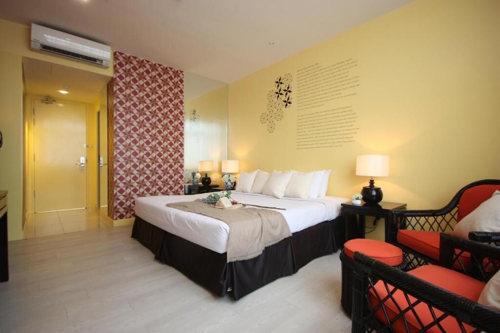 A hotel room with a bed, two bedside tables, a chair, and a wall with text and a decorative design.