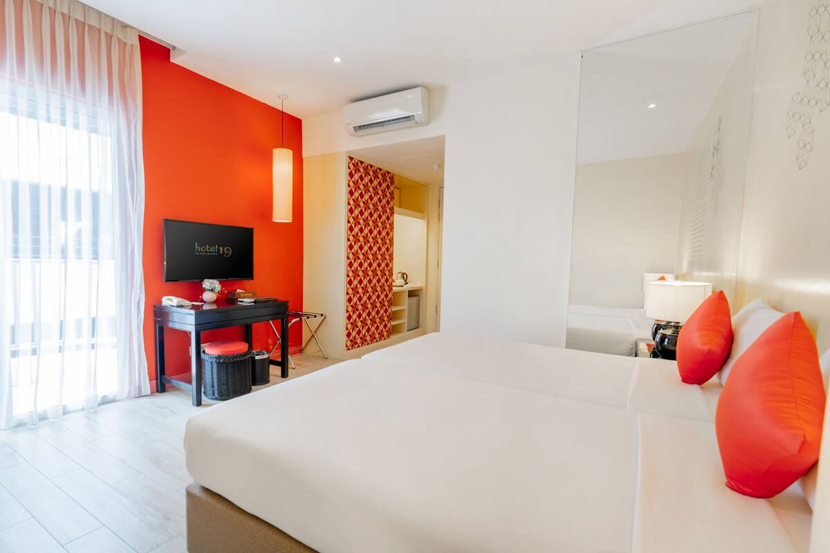 Habitación de hotel con una cama grande, un escritorio con silla, televisión y ventana con cortinas.