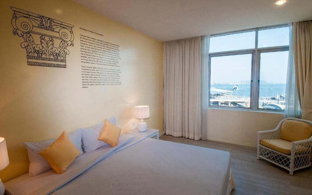 Une chambre d’hôtel avec un grand lit, une chaise, une fenêtre donnant sur la ville et un élément décoratif mural.