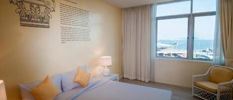 Une chambre d’hôtel avec un grand lit, une chaise, une fenêtre donnant sur la ville et un élément décoratif mural.