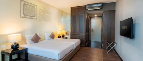 Habitación de hotel con una cama grande, dos mesitas de noche con lámparas, un televisor montado en la pared y suelo de madera.