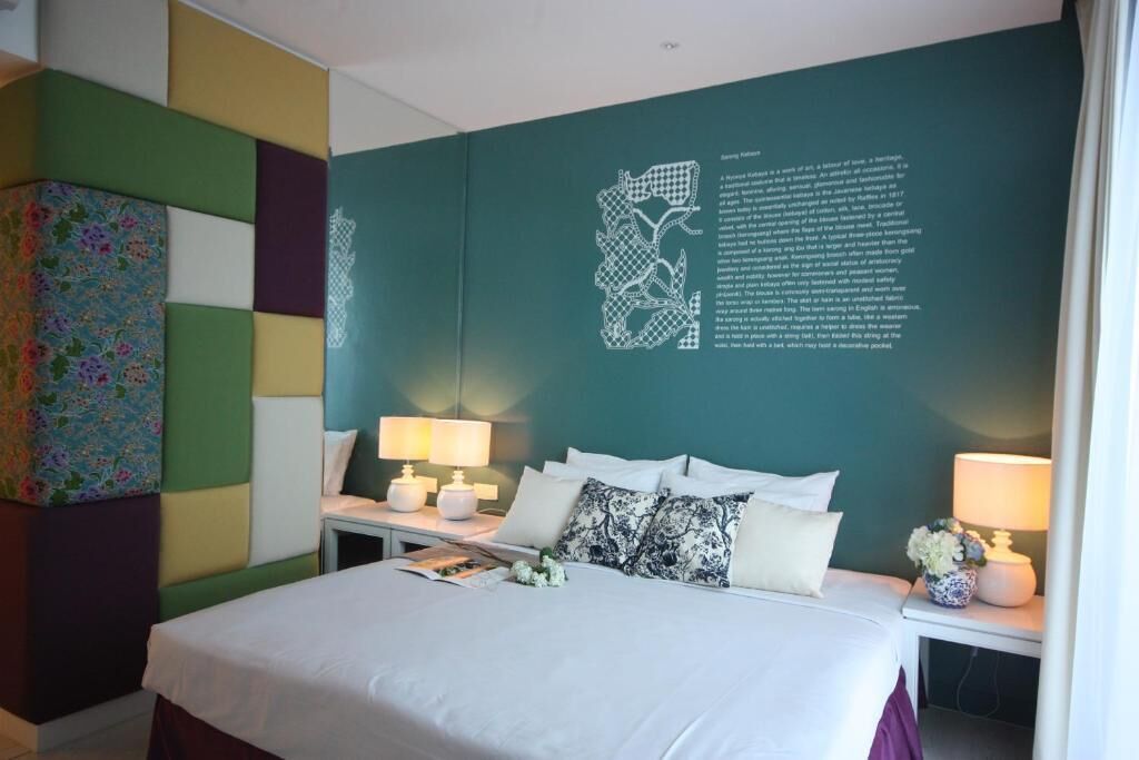 A modern hotel room with a large bed, two bedside tables with lamps, a decorative wall piece, and a colorful abstract painting.