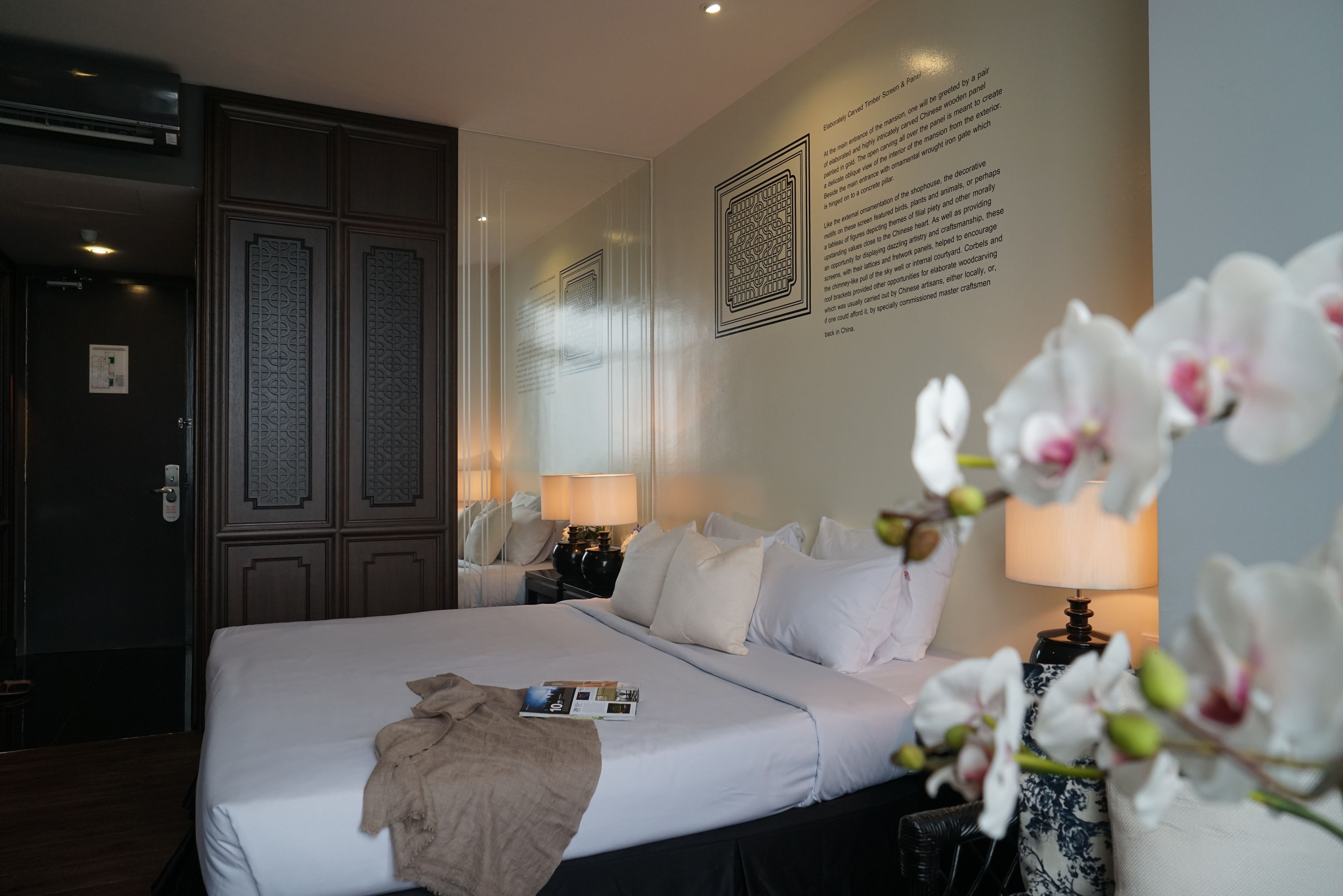 A neatly arranged hotel room with a large bed, a nightstand with a lamp, and a wall with decorative panels.