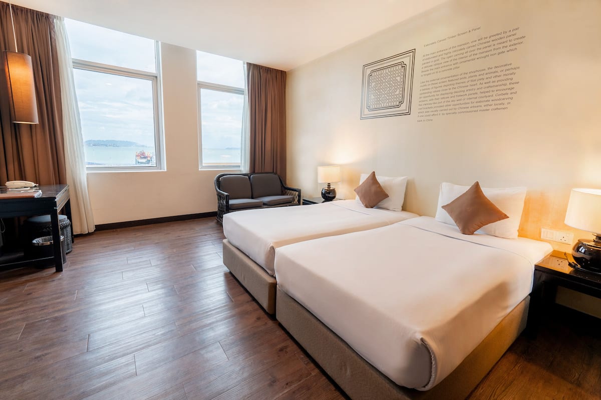 Habitación de hotel con dos camas, un escritorio, una silla y un ventanal con vistas.