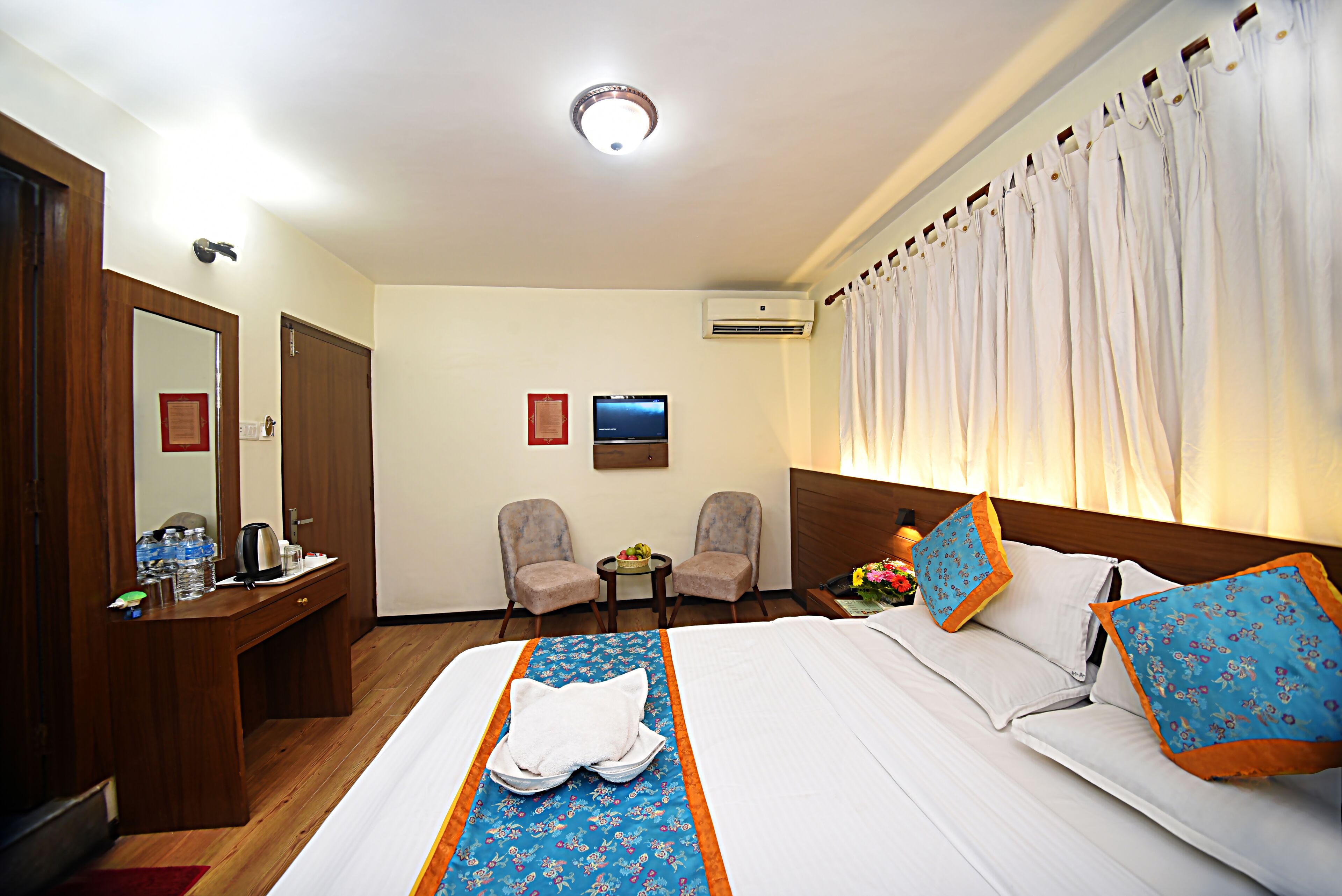 Ein Hotelzimmer mit einem Bett, zwei Stühlen, einem Schreibtisch mit Spiegel und einer Klimaanlage.