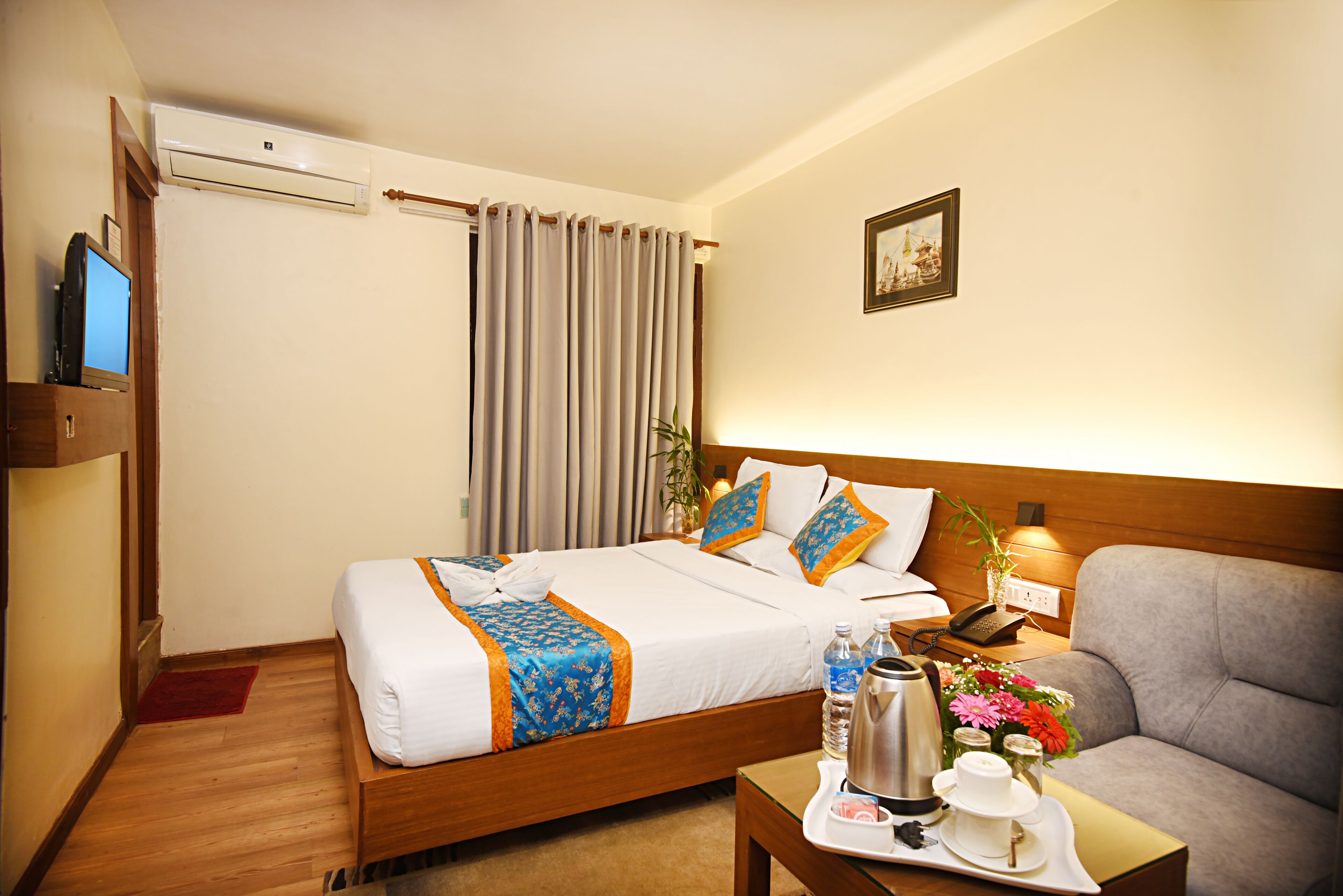 A hotel room with a bed, a sofa, a coffee table, a TV, and a picture on the wall.