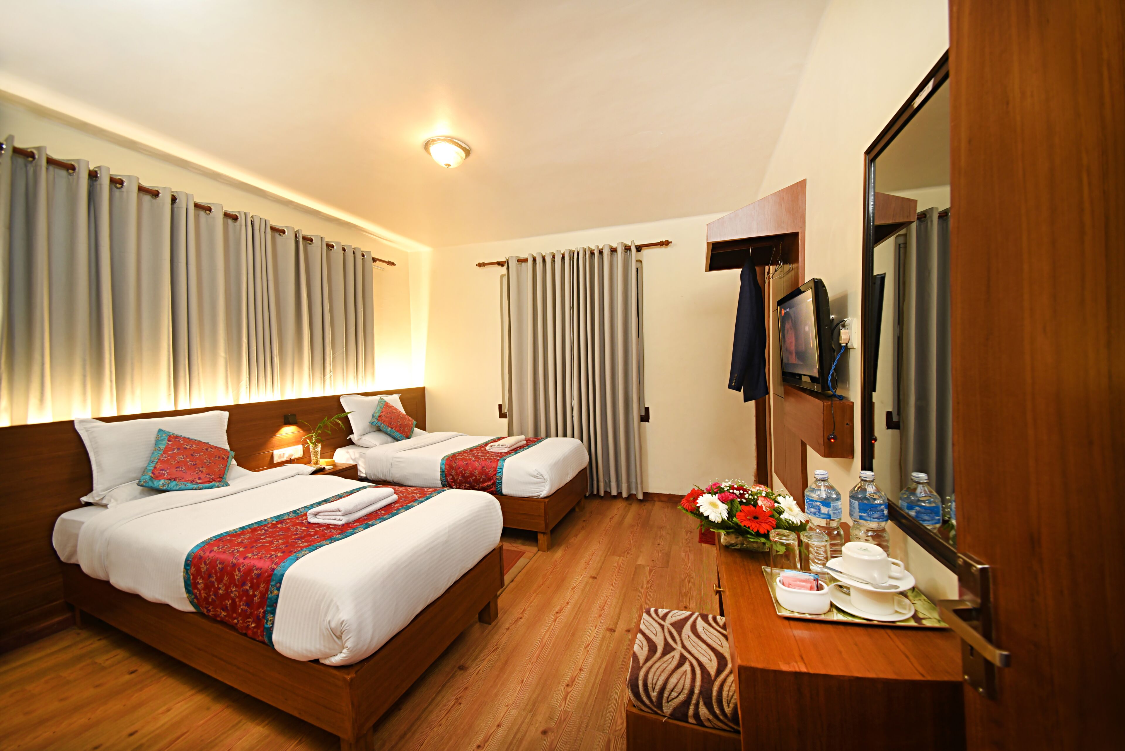 A hotel room with two beds, a wooden desk, a mirror, and a bathroom visible through an open door.