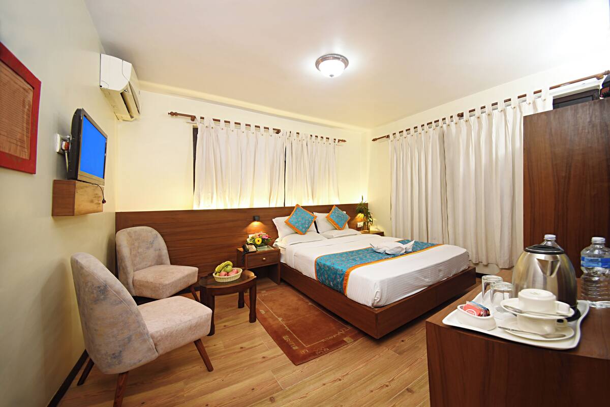 A hotel room with a wooden bed, a desk with a tray of breakfast items, a chair, and a television on a wooden stand.